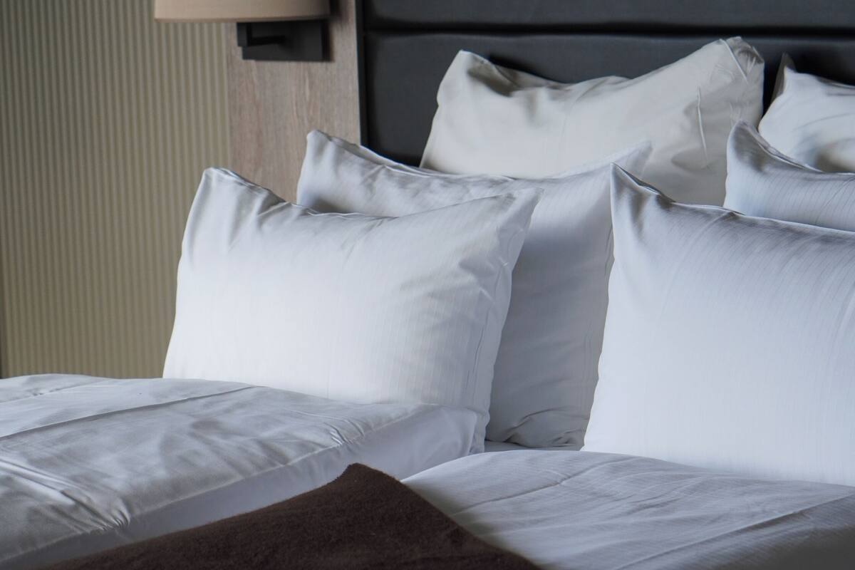 A neatly made bed with white linens and a brown throw blanket.
