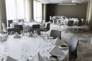 Un salón de conferencias con mesas redondas dispuestas para cenar, equipado con sillas, platos, cubiertos y copas de vino.