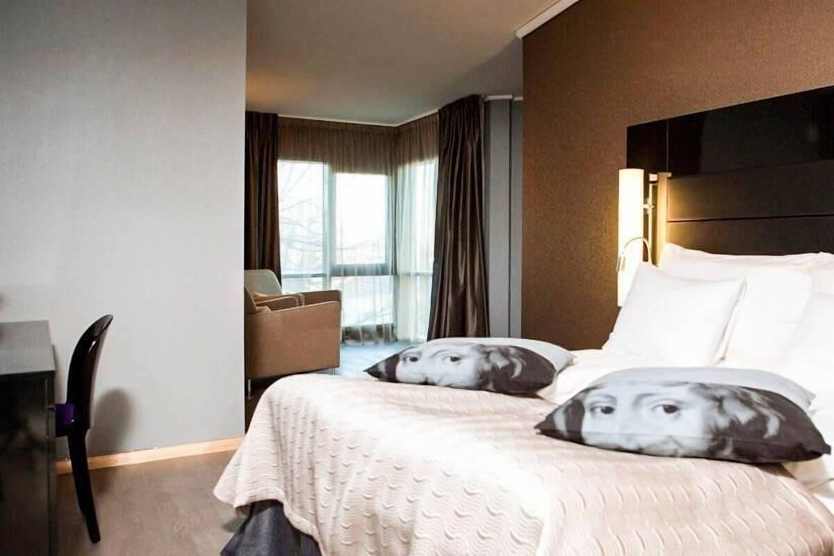 A hotel room with a bed, two pillows, a chair, and a desk.