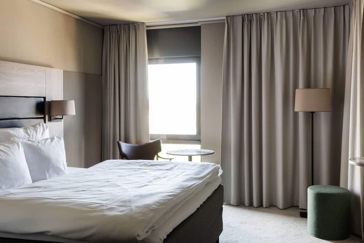 A hotel room with a bed, a chair, a small round table, and a lamp.