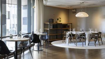 A modern dining area with round tables and chairs, a bookshelf, and pendant lighting.