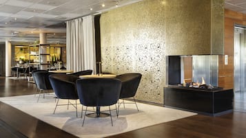 A modern lobby with a seating area featuring black chairs and a central table, a textured wall, and a fireplace with a visible fire.
