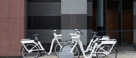 Tres bicicletas blancas estacionadas frente a un edificio de diseño moderno, con una combinación de paneles oscuros y claros.