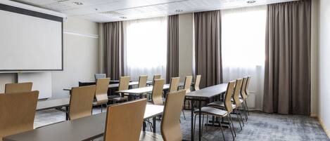 A conference room with a whiteboard, projector, and large windows with curtains.