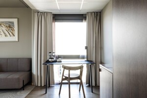 Una habitación moderna con un sofá, una mesa de comedor con una silla, una ventana con cortinas y un cuadro en la pared.