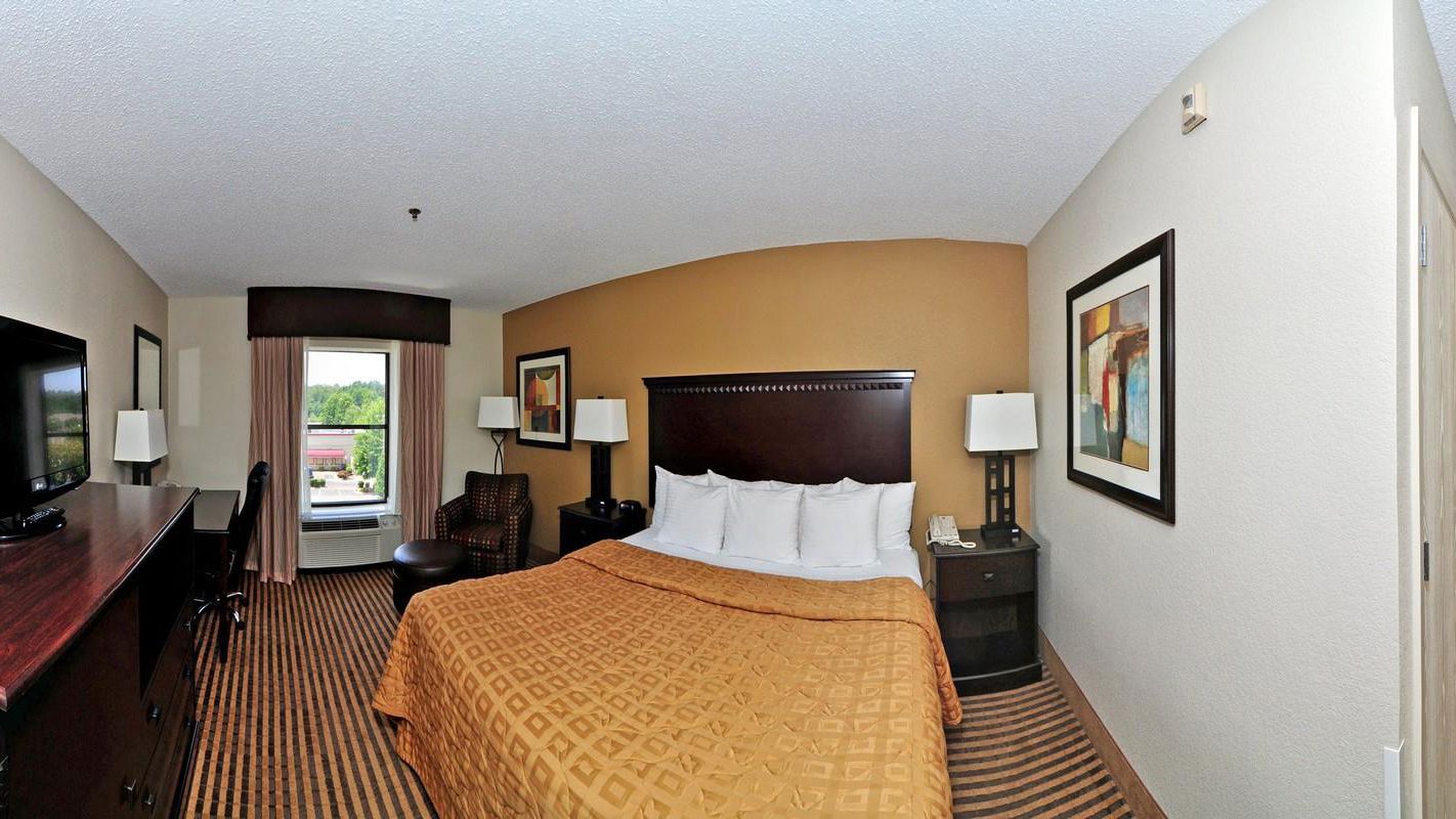 A hotel room with a large bed, a desk, a chair, a TV, and a window with curtains.