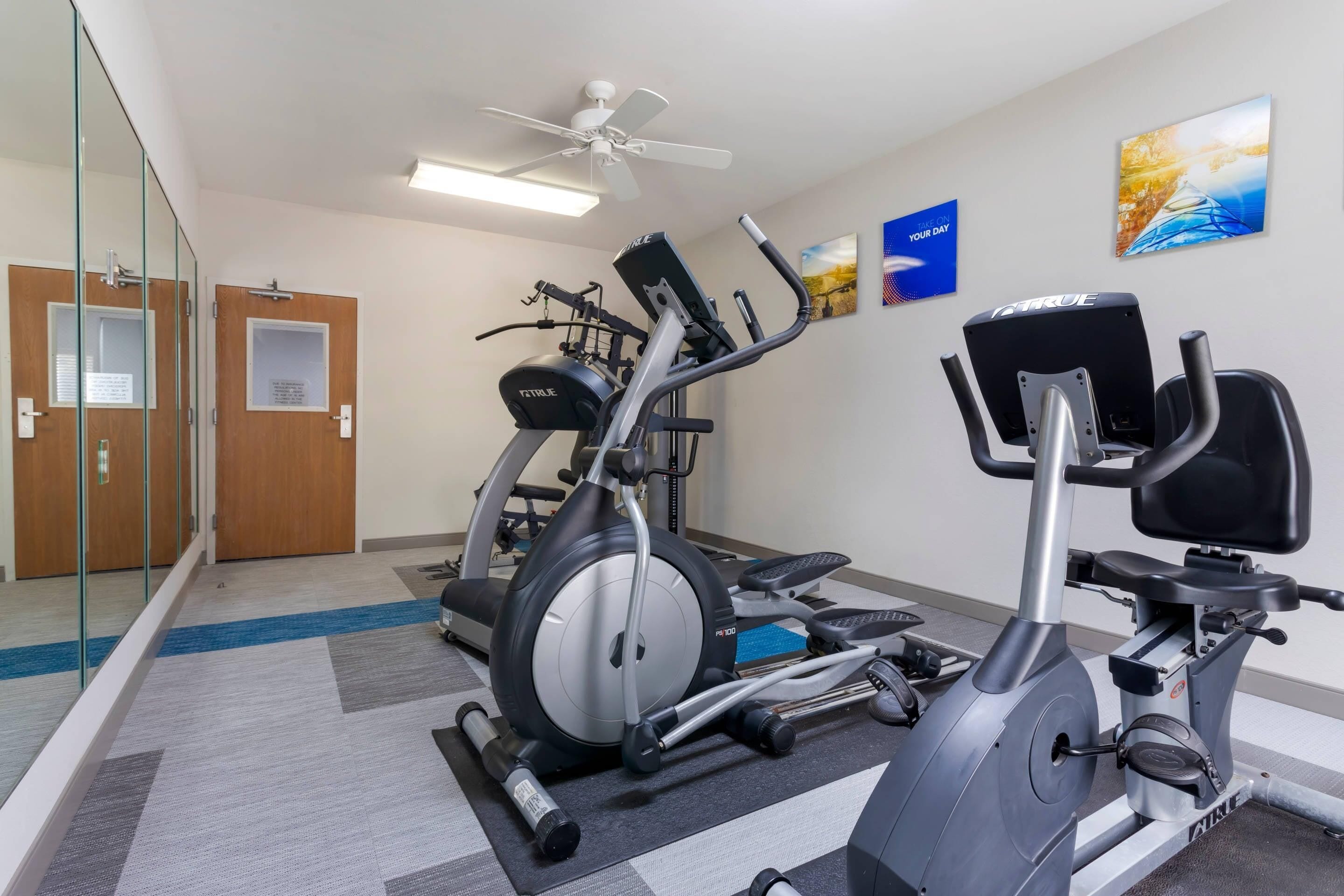 A fitness room with cardio equipment, a ceiling fan, and motivational posters.