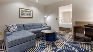 Ein Hotelzimmer mit einer Eckcouch, einem runden Tisch, einem Schreibtisch und einem Bett.