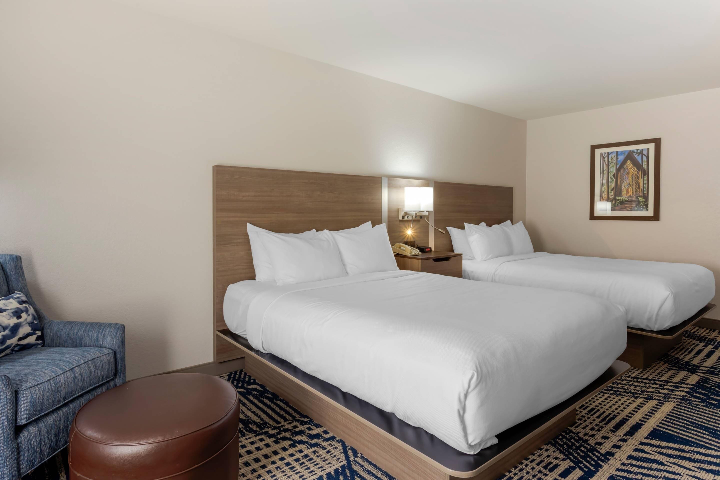A hotel room with two beds, a desk, a chair, and a small ottoman.