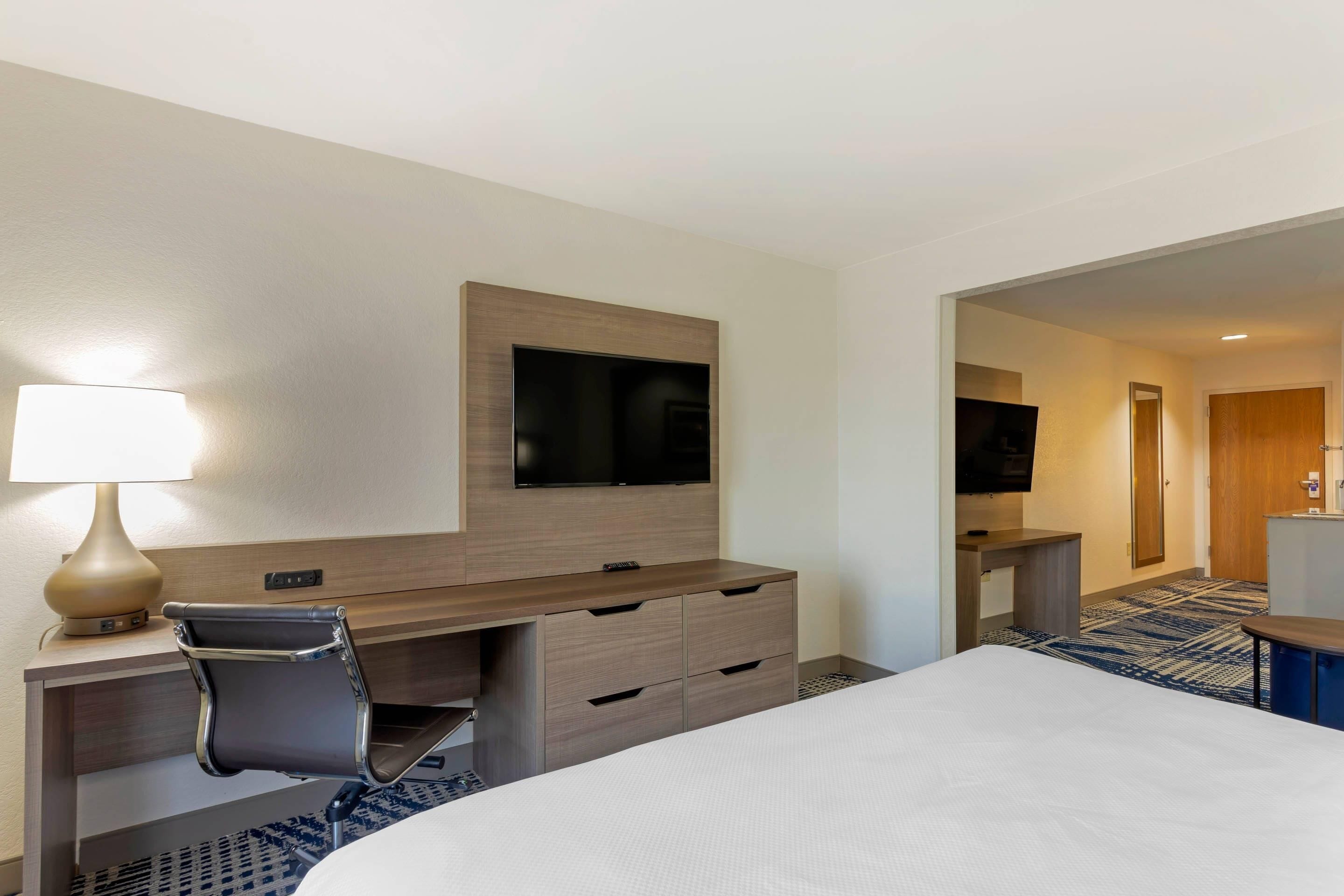 Une chambre d’hôtel comprenant un lit, un bureau avec une chaise, un téléviseur fixé au mur et une lampe.