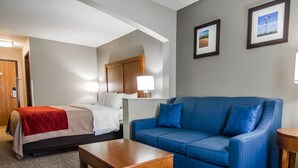 Un cuarto de hotel con una cama, un sofá azul, una mesita de madera y dos cuadros en la pared.