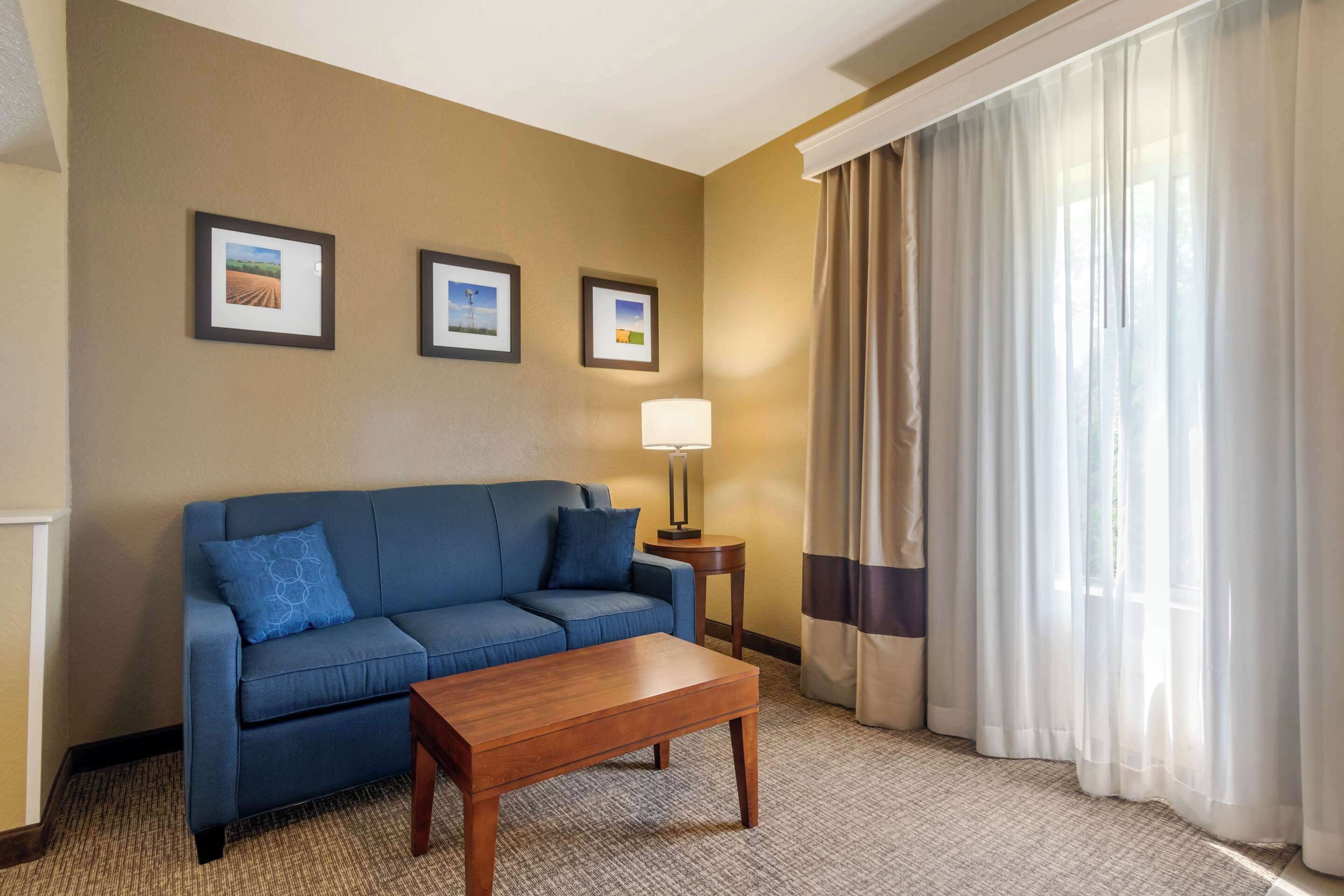 A hotel room with a blue sofa, a wooden coffee table, and a lamp. There are three framed pictures on the wall.