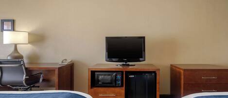 A hotel room with two beds, a television, a microwave, a refrigerator, a desk with a lamp, and a chair.