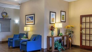 Un hall con dos sillones azules, una consola de madera con un florero y cuadros enmarcados en la pared, además de una puerta con un panel de vidrio.