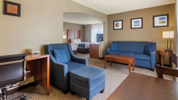 Una habitación de hotel con una cama, dos sofás azules, un escritorio de madera, una mesita pequeña y una lámpara.