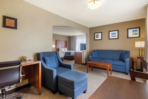 Een hotelkamer met een bed, twee blauwe sofa's, een houten bureau, een bijzettafeltje en een lamp.