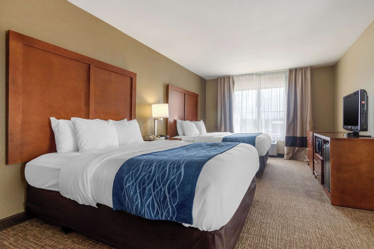 A hotel room with two beds, a desk, a television, and a window with curtains.