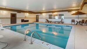 Una piscina interior con agua cristalina, un indicador de profundidad de 1.2 metros y un indicador de anchura de 3.6 metros. Hay sillas de descanso y una mesa con sombrillas junto a la piscina.