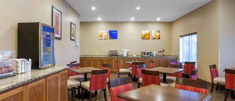 A restaurant with wooden tables and chairs, a kitchen area, and framed pictures on the wall.