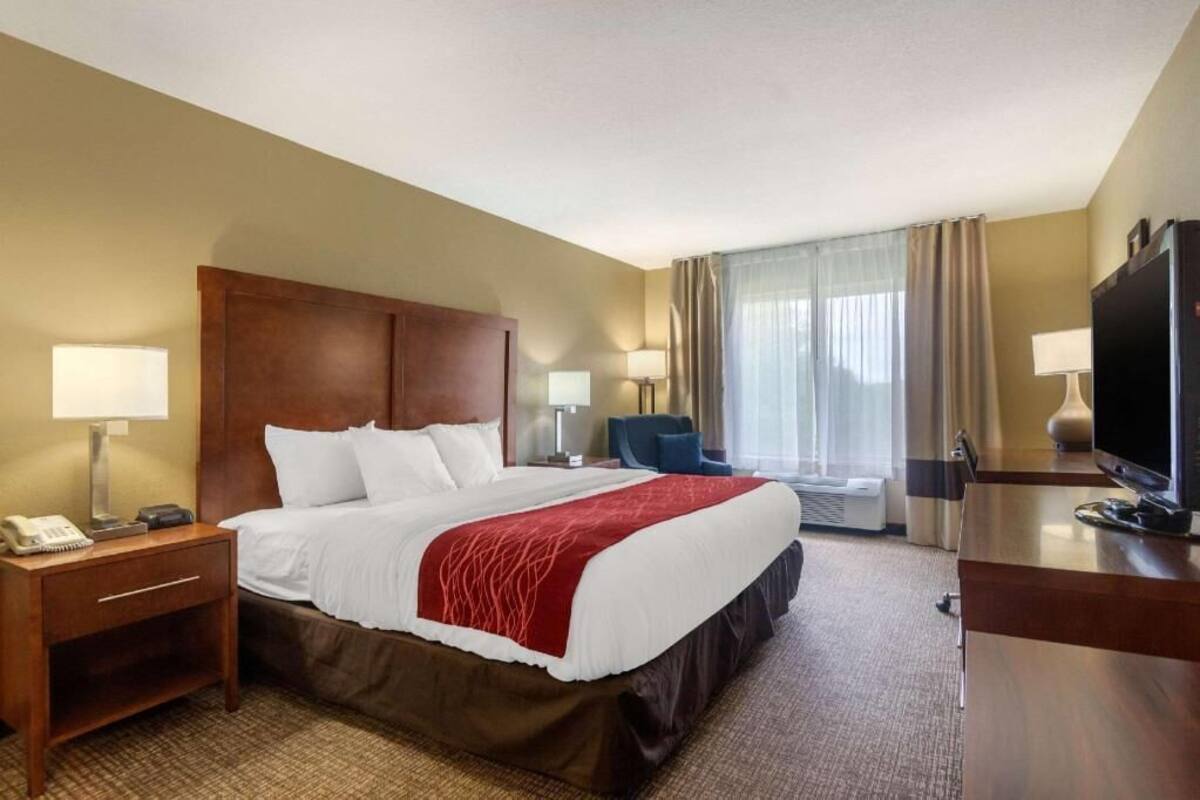 A hotel room with a bed, bedside tables, a desk with a TV, and a chair.