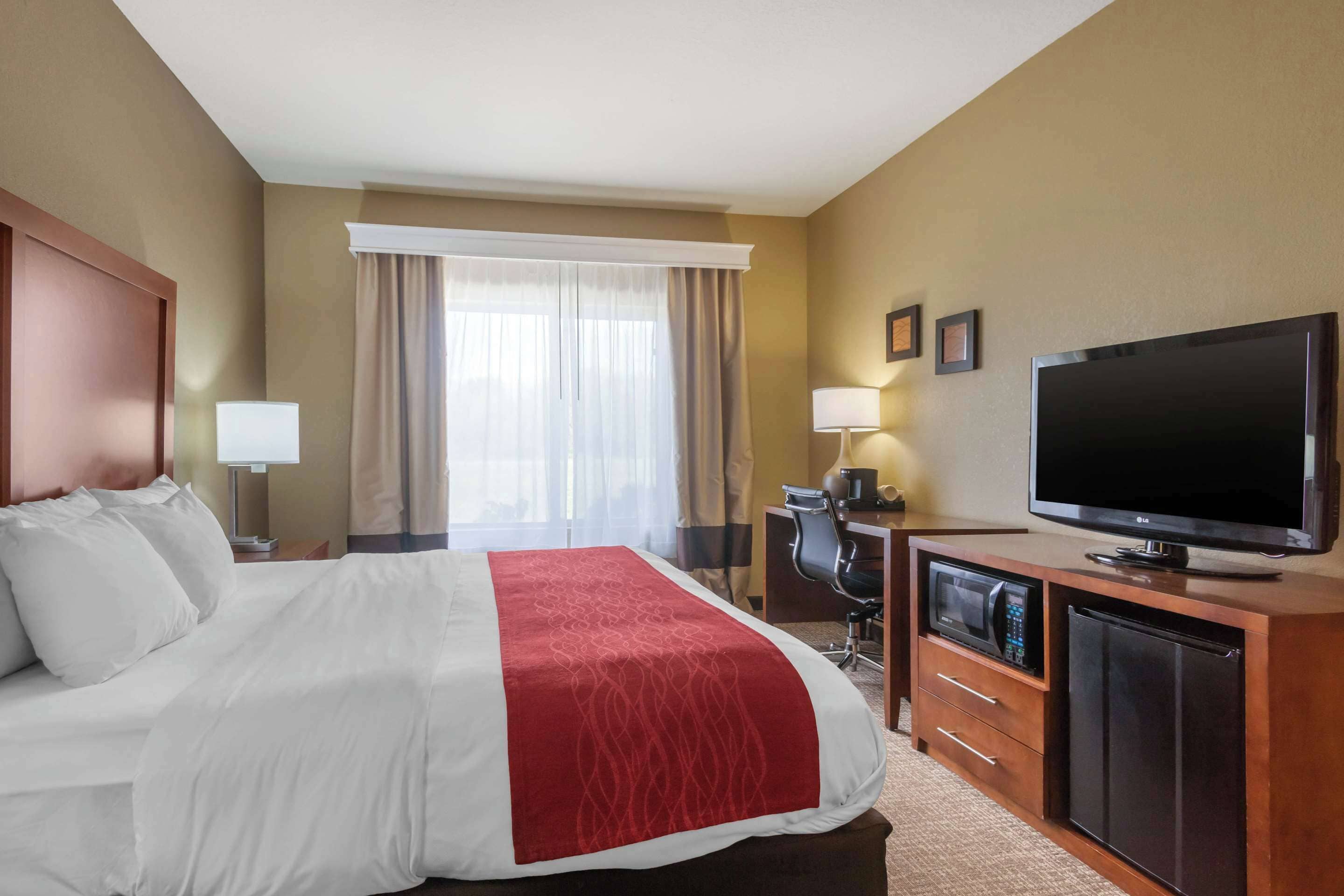 Una habitación de hotel con cama, escritorio con computadora, televisión y microondas.