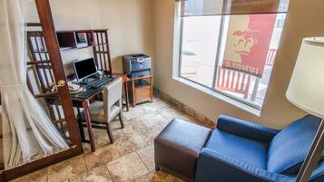 A compact room with a desk, computer, printer, and a window with a view of a balcony.