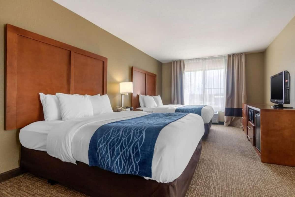 A hotel room with two beds, a desk, a television, and a window with curtains.