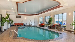 Una piscina interior con suelo de baldosas, techo de madera y zona de estar con cojines naranja.