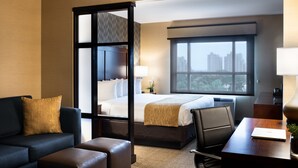Habitación de hotel con cama con dosel, un escritorio con una computadora portátil, un sofá y vista a la ciudad por la ventana.