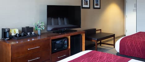A hotel room with a TV, a desk with a coffee maker, a microwave, a bed with a red blanket, and two framed pictures on the wall.