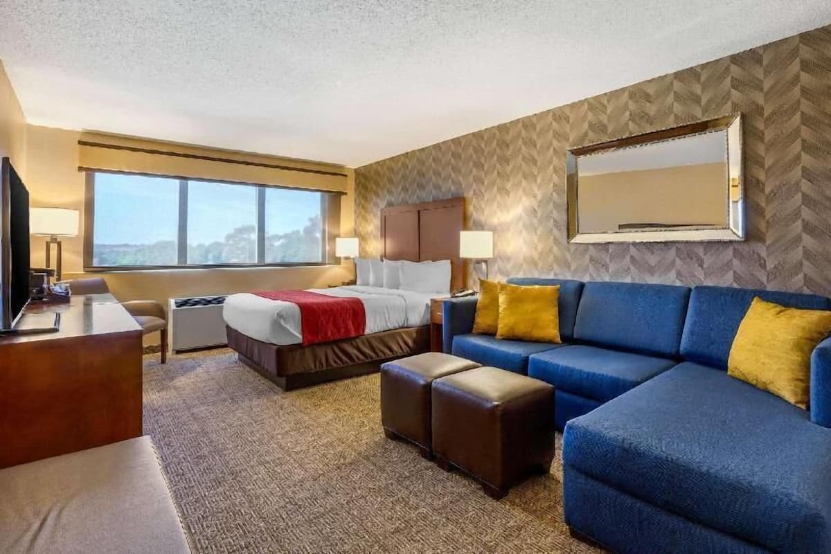 A hotel room with a bed, a sofa, a desk, a TV, and a large window.