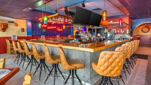 Zona de bar con una barra larga, varios taburetes y un letrero de neón.