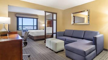 Una habitación de hotel con cama, sofá, reposapiés, escritorio y silla.