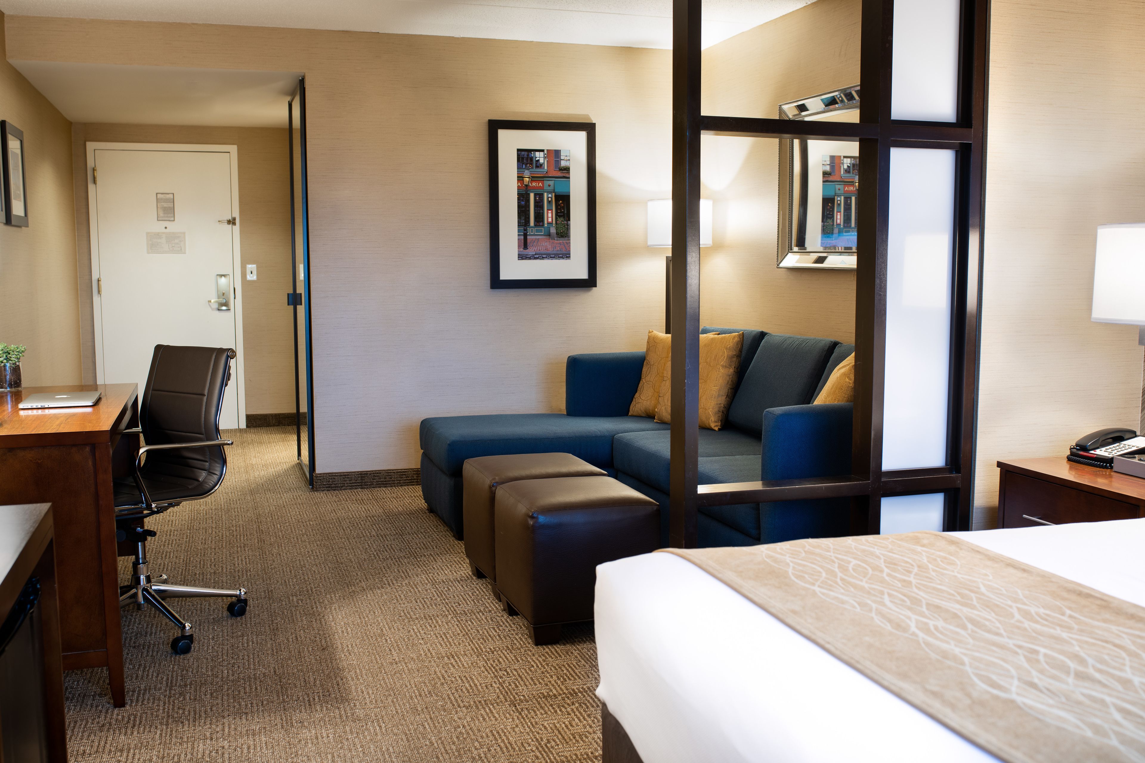 Une chambre d’hôtel comprenant un lit, un bureau avec une chaise, un canapé et une petite table avec une lampe.