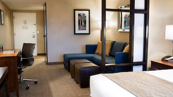 A hotel room with a bed, a desk with a chair, a sofa, and a small table with a lamp.