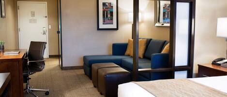 Une chambre d’hôtel comprenant un lit, un bureau avec une chaise, un canapé et une petite table avec une lampe.