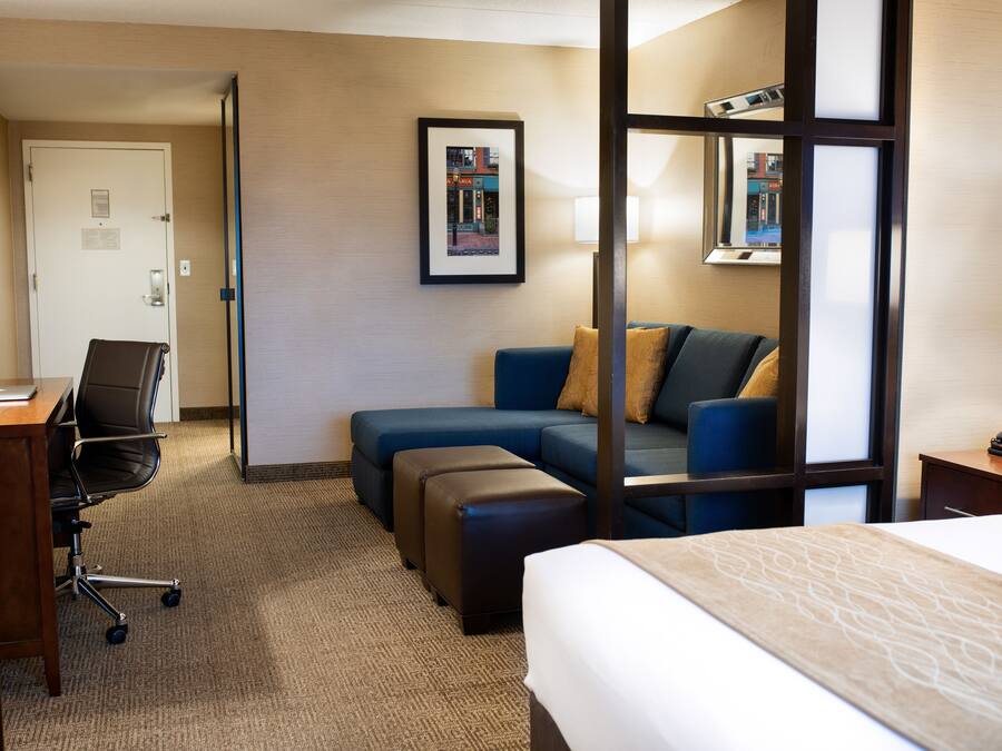 A hotel room with a bed, a desk with a chair, a sofa, and a small table with a lamp.