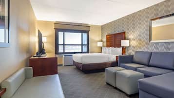 Una habitación de hotel con cama, sofá, escritorio con lámpara, televisión y un ventanal grande.