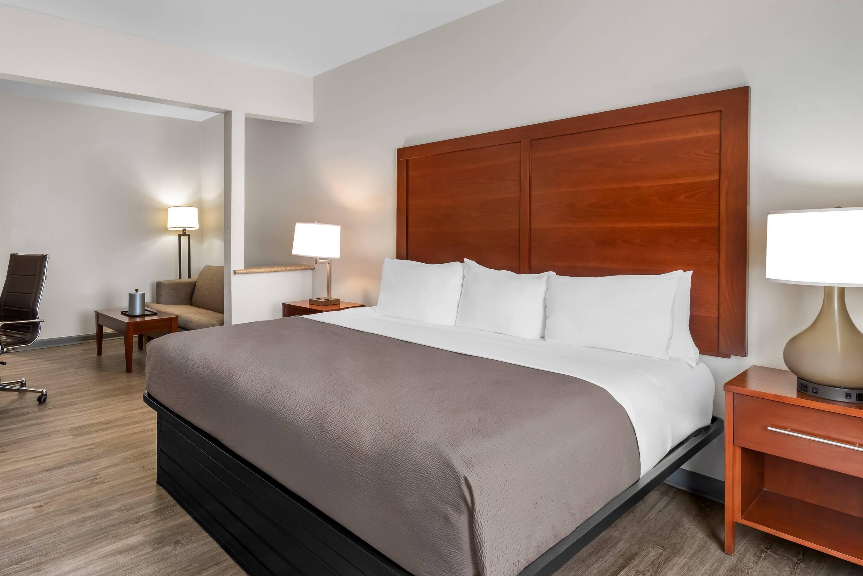 A hotel room with a large bed, a desk, a chair, and a lamp.