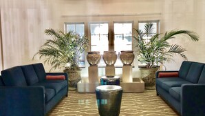 Eine Lobby mit zwei blauen Sofas, einem gemusterten Teppich und großen Kübelpflanzen.
