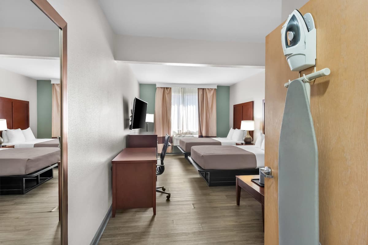 Quarto de hotel com escrivaninha, duas camas, televisão e espelho.