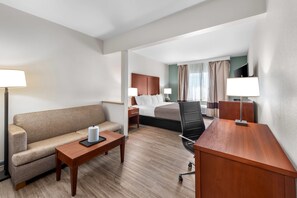 A hotel room with a bed, a sofa, a desk, a chair, and a nightstand. - Quality Suites Waldorf (Waldorf)
