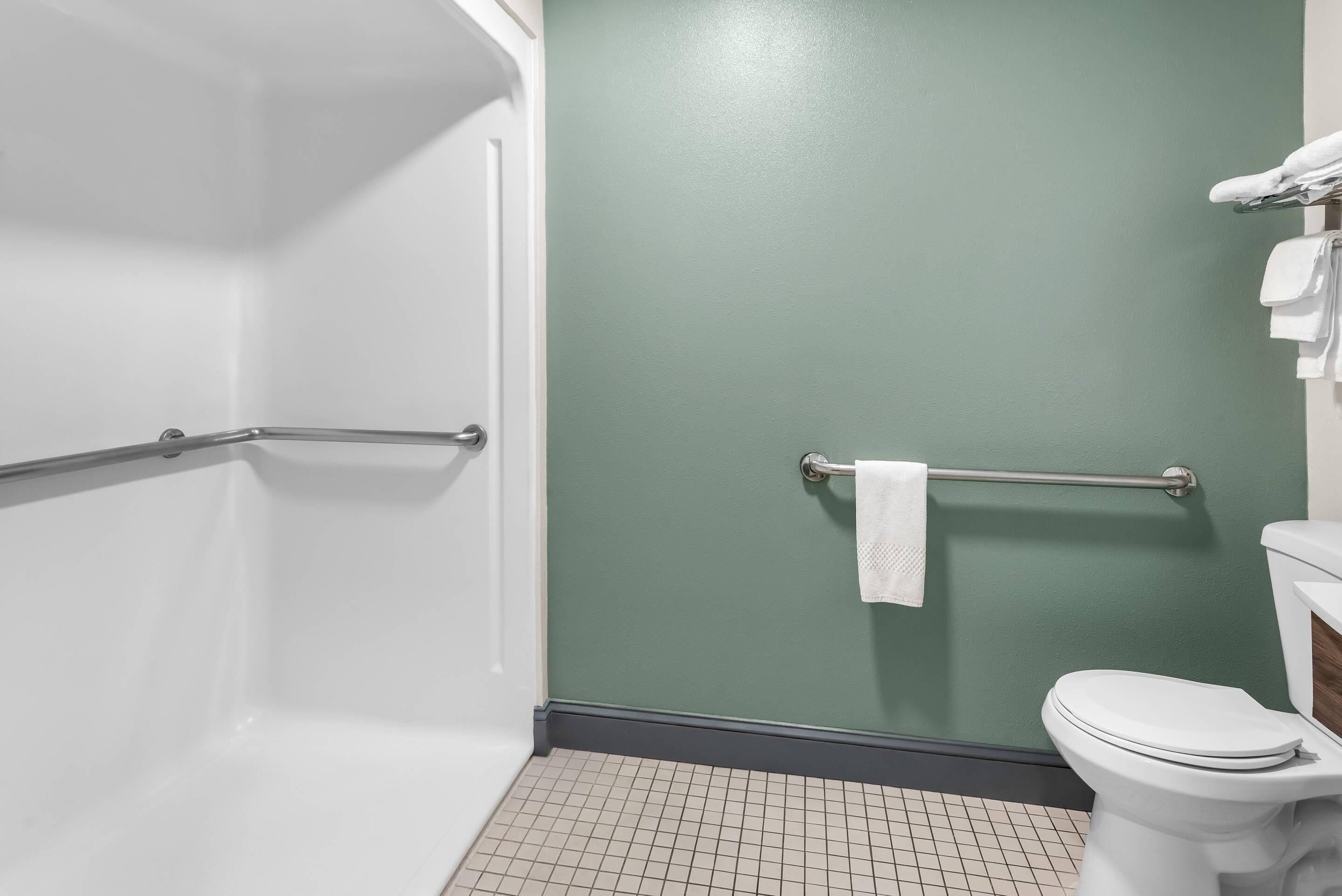 A bathroom with a white toilet, a grab bar, a towel rack, and a green wall.