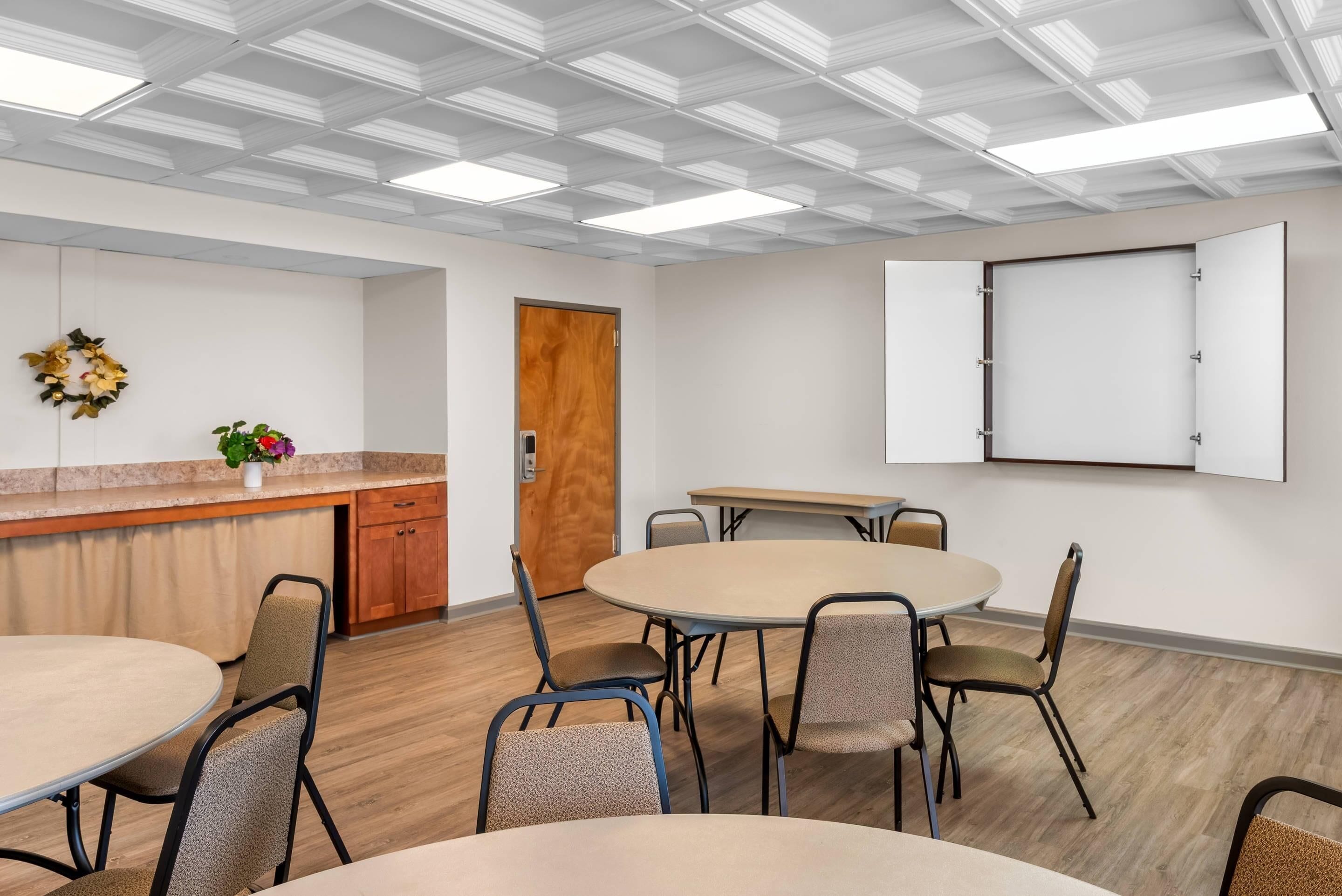 Un salón de conferencias con una mesa redonda, sillas, una pizarra y una puerta de madera.