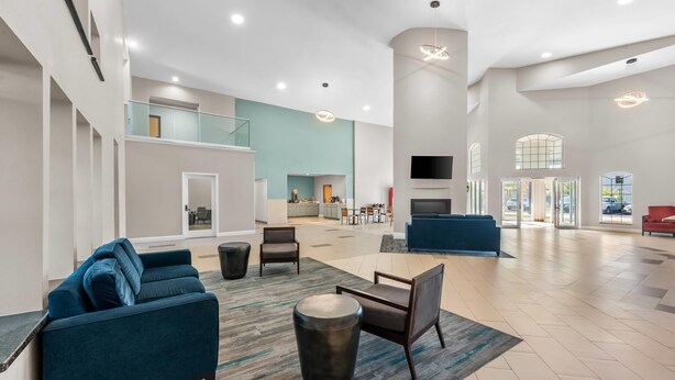 Eine geräumige Lobby mit einem blauen Sofa, einem runden Couchtisch und einem an der Wand befestigten Fernseher.