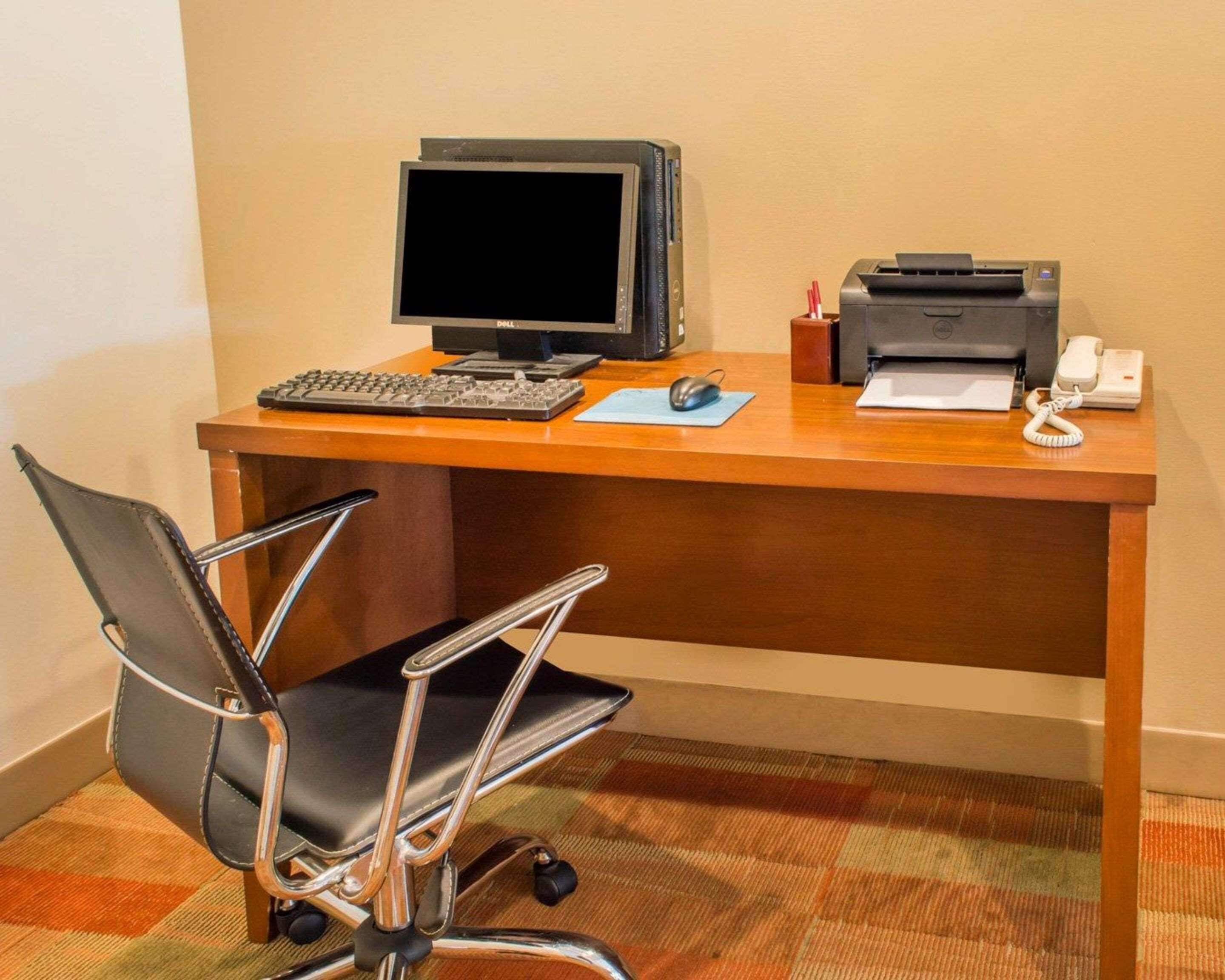 A hotel workspace with a desk, computer, printer, telephone, and office chair.