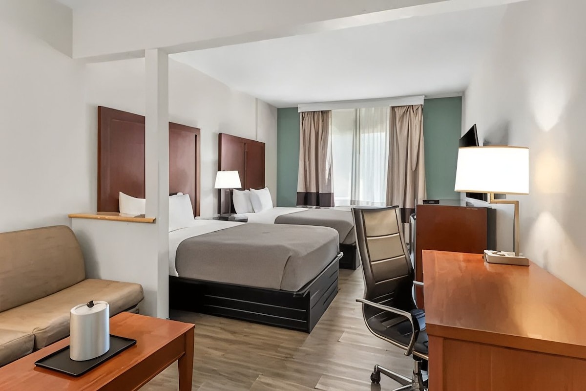 A hotel room with two beds, a sofa, a desk, and a chair.