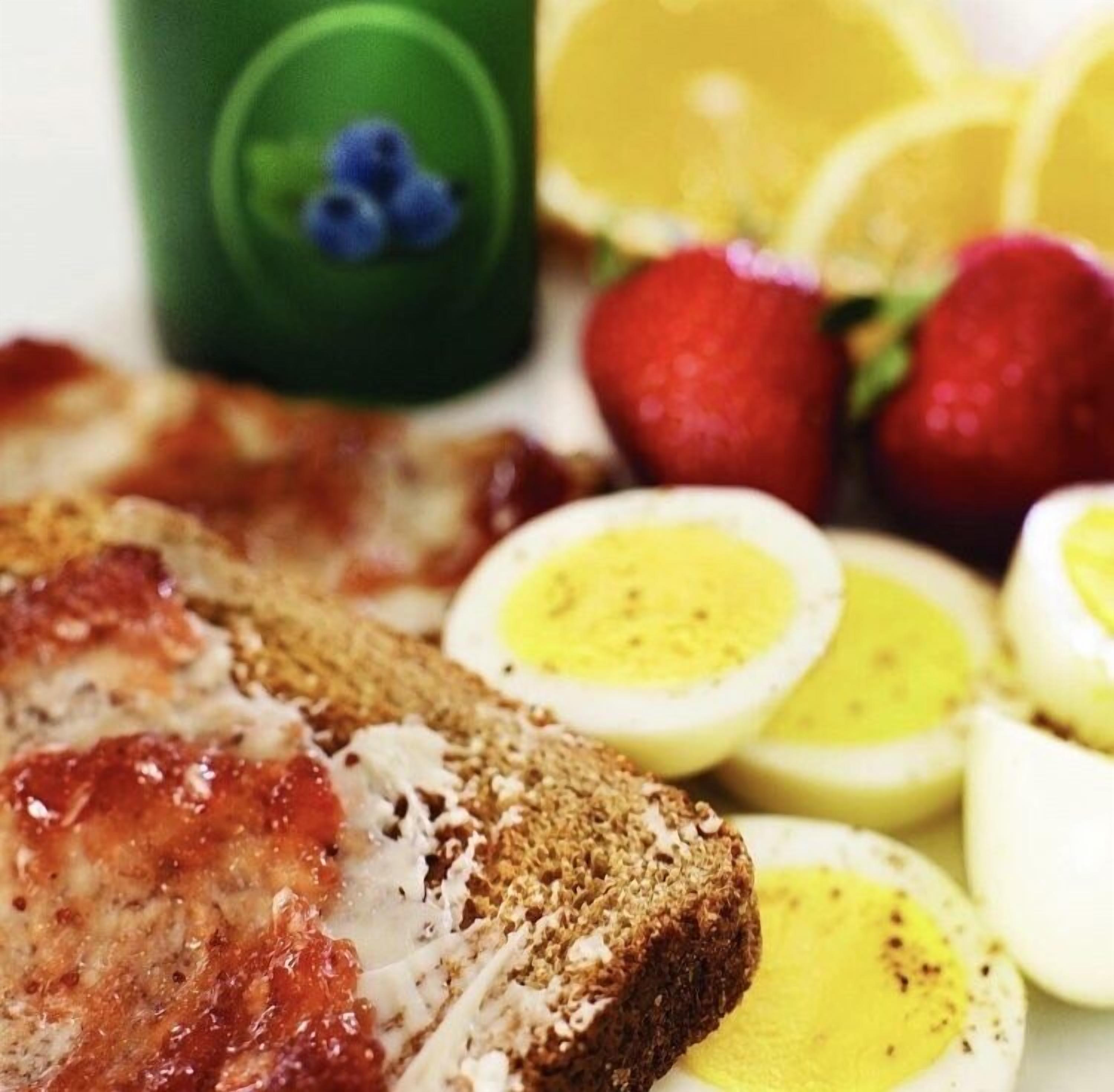Un plato de desayuno con tocino, huevos, fresas y una taza verde con arándanos.