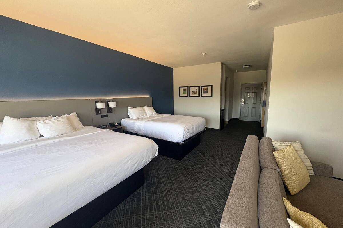 Ein Hotelzimmer mit zwei Betten, einem Sofa und einem Flur, der zu einem weiteren Zimmer führt.