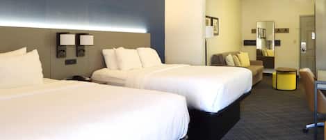 Una habitación de hotel con dos camas, un sofá, una mesita y un espejo.